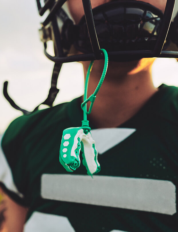 closeup of an athletic mouthguard hanging from a young football player's helmet