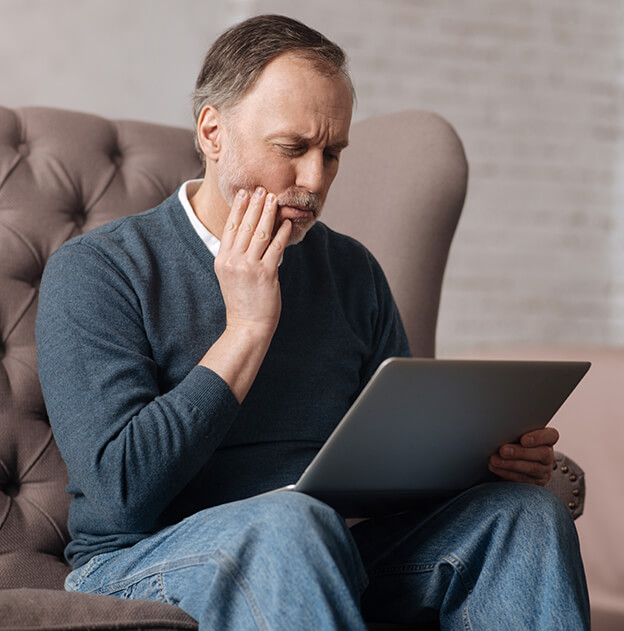 man holding his jaw in pain while looking at his laptop