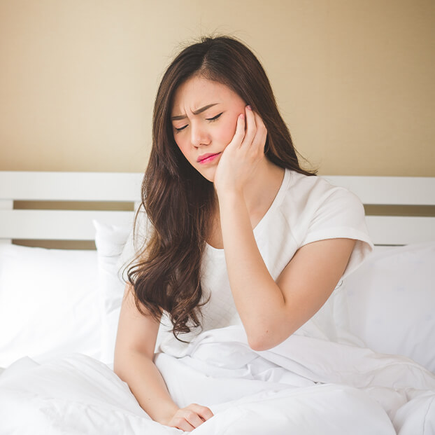 woman sitting up in bed, holding her jaw in pain