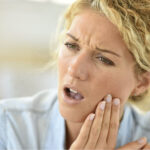 woman holds her jaw in pain with a TMJ disorder
