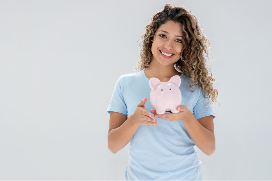 young woman holds a piggybank and smiles after learning about affordable dentistry