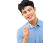 young man smiles and holds up his clear aligner to straighten his teeth