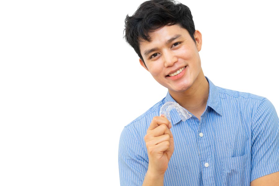 young man smiles and holds up his clear aligner to straighten his teeth