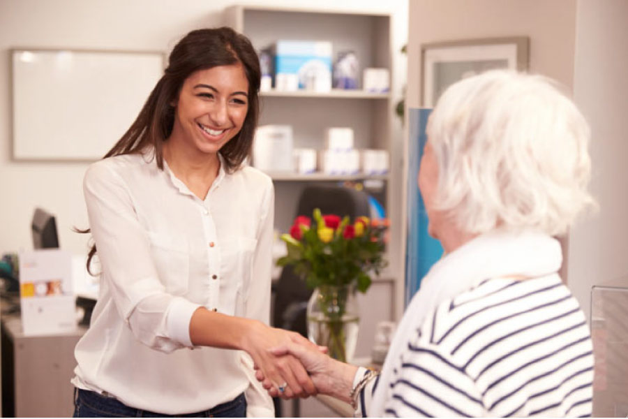 senior woman is greeted warmly by dental employeer,