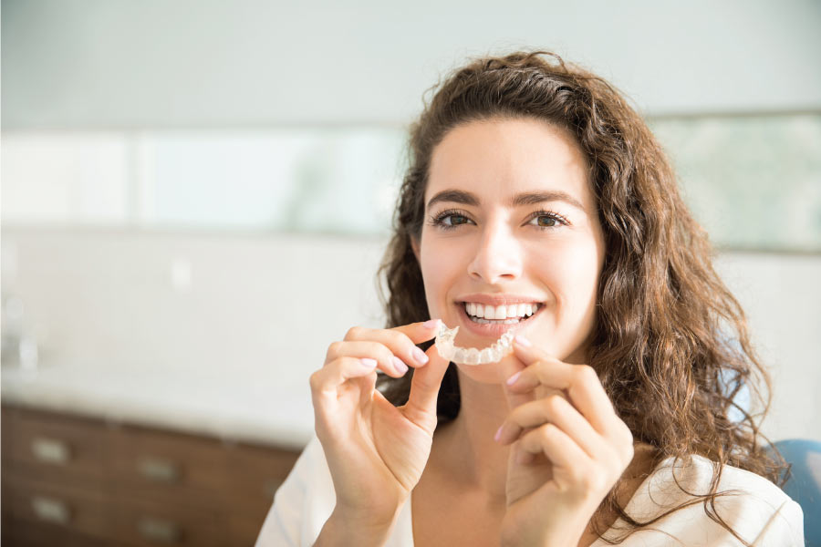 woman smiles and holds her clear aligner up to her mouth
